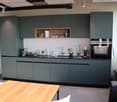 modern kitchen with wooden table, green cabinets, white walls, large window, sink, oven, countertop, trash bin