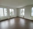 Empty room with white walls, brown floor, three windows, and radiators