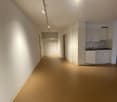 Empty room with white walls, brown floor, kitchen area with sink and cabinets