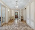 Spacious foyer with marble tile flooring, white paneled walls, a chandelier, and a wooden front door with glass panes. The foyer leads to other rooms in the home.
