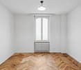 Empty room with white walls, hardwood herringbone flooring, a window, and a ceiling light fixture.