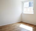 Empty room with white walls, hardwood flooring, and a large window providing natural light