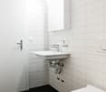 white bathroom with sink, toilet, mirror and white tile flooring