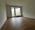 Empty room, wooden floor, white walls, large glass doors leading to balcony, central heating, electrical outlet