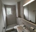 Bathroom with tile flooring, mirror, white sink, toilet, shower, light above mirror