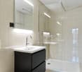 Modern bathroom with white tiles, white sink, black cabinet, and a shower stall
