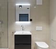 Modern bathroom with white tiles, black vanity unit with sink, wall-mounted toilet, and recessed lighting above the mirror.