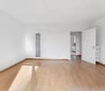 Empty room with wooden floor, white walls, two doors, and a window.