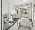 modern kitchen with white cabinets, black countertops, stainless steel sink, dishwasher, microwave, and a window with a view of trees