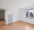 Empty room with white walls, wooden floor, white radiator, window with view outside