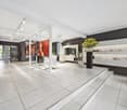 modern salon with white tiled floor, white walls, large windows, white chairs, shelves with products, large posters, glass partitions, plants