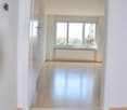 Empty room with wooden floor, white walls, large window, and a white door.