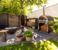 Outdoor fireplace, tree, potted plants, logs, wooden chairs, wooden fence, gravel floor