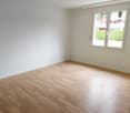 Spacious bedroom with hardwood flooring, white walls, and large windows providing natural light.