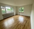 Spacious room with hardwood flooring, large windows providing natural light, and radiators along the walls.