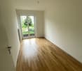 Spacious room with hardwood flooring, white walls, and a sliding glass door leading to a balcony or terrace.