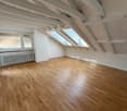 empty room with wooden floor and white walls, two attic windows, white wooden beams, a white radiator