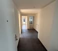 Empty hallway, white walls, black tiled floor, open doors leading to rooms