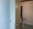 The image shows a bathroom with a toilet, a small space, and a door leading to the room.