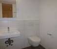 white tile walls, white toilet, white sink, silver faucet, silver wall mounted soap holder, large mirror