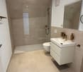 modern bathroom, beige tiles, shower, toilet, white vanity, mirror, underfloor heating