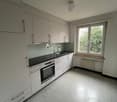 empty modern kitchen, black counter, white cabinets, white drawers, glass window, white floor