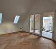 Empty room with wooden floor, two windows, sliding glass doors leading to a balcony