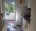 white cabinets, white countertop, open door to balcony, white tile wall, open oven, sink with faucet, light colored floor