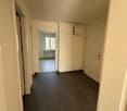 Empty hallway with white walls, wooden floor, white cabinets, and a window.
