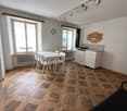 open dining area, parquet flooring, white walls, large window, dining table, four chairs, radiator, clock, kitchen area, kitchen cabinets, countertop, folding bed