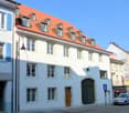white building, red roof, multiple windows, wooden door, metal gate, street light, parking sign