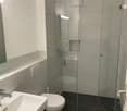 modern bathroom with white tiles, glass shower enclosure, white toilet, white sink, silver faucet, black cabinet