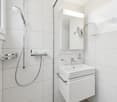 modern bathroom with white tiles, shower, sink, mirror, and a window