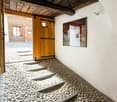 Stone steps leading to a wooden door, white walls, wooden ceiling, a wall mirror reflecting the interior, a wooden building in the background