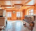 Spacious room with wooden walls and ceiling, large windows, ornate fireplace, and a grand piano covered in a white sheet