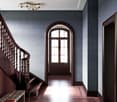 Wooden staircase with handrail, patterned tiles at the bottom, arched window, wooden door, and decorative ceiling light