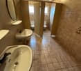 Two sinks, two toilet stalls, tiled flooring, wooden ceiling, two lamps