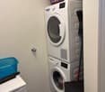 Laundry room with stacked washing machine and dryer, storage boxes, and a basket on top of the dryer
