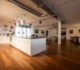 Open kitchen with island, wooden floor, white walls, large windows, dining table, chairs, artwork on the wall, pendant lights