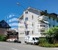 3 story building, white exterior, multiple balconies, street light, parked van, parked car