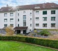 3 story white building, brown roof, green shutters, raised ground floor, garden, gravel path