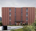 Modern building with brown facade, multiple windows, entrance with wooden swing, children's play area, underground garage
