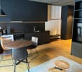 modern kitchen with dark cabinetry, wooden dining table, 4 modern chairs, tv, wooden bench