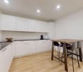 modern kitchen with a wooden table, white cabinets, wooden floor, black countertops, built-in oven and coffee machine
