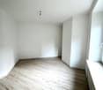 an empty room with wooden floors, white walls, and a window with a bench, no furniture or visible features