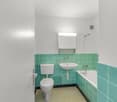 modern bathroom with turquoise tiles, white toilet, white sink, bathtub, mirror, shower head, faucets