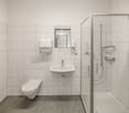 white tiled walls, white toilet, white sink, glass shower enclosure, mirror, soap dispensers