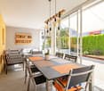 Modern open dining room with large table and chairs, sliding doors to terrace, view of garden, pendant lights, and modern decor