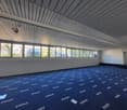 Empty room, blue carpet, white walls, windows with metal grilles, ceiling with wooden slats