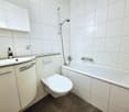 white tiles, bathtub, toilet, sink, shower head, white cabinets